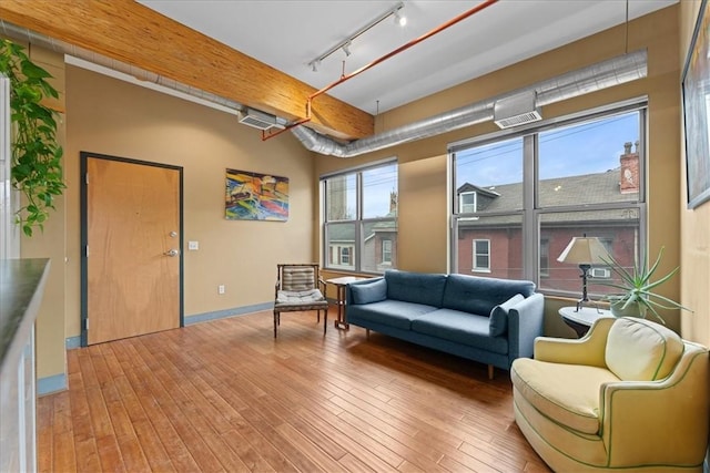 living area with rail lighting, beam ceiling, baseboards, and hardwood / wood-style floors