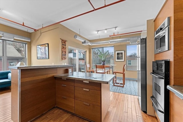 kitchen featuring brown cabinetry, modern cabinets, stainless steel appliances, and light wood finished floors