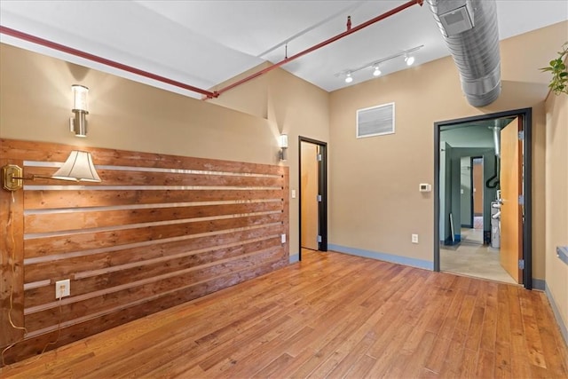 spare room featuring light wood-type flooring, rail lighting, visible vents, and baseboards