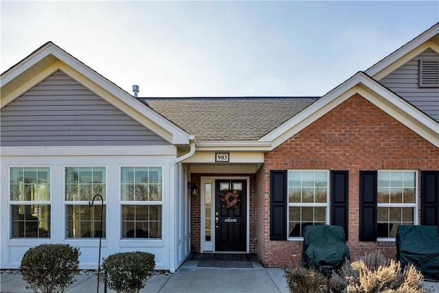 entrance to property featuring brick siding and roof with shingles