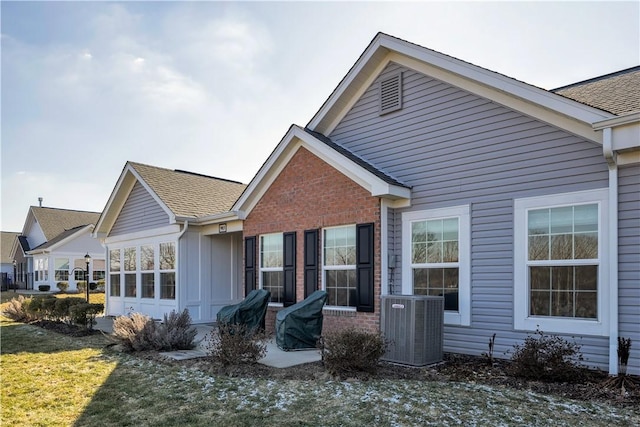 back of house featuring a yard, central AC unit, a shingled roof, and brick siding