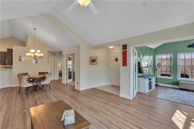 unfurnished living room featuring vaulted ceiling, light wood finished floors, ceiling fan with notable chandelier, and baseboards