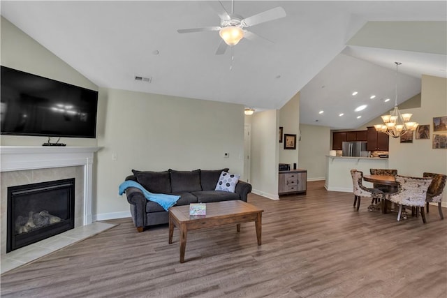 living room featuring a tile fireplace, ceiling fan with notable chandelier, visible vents, baseboards, and light wood-style floors