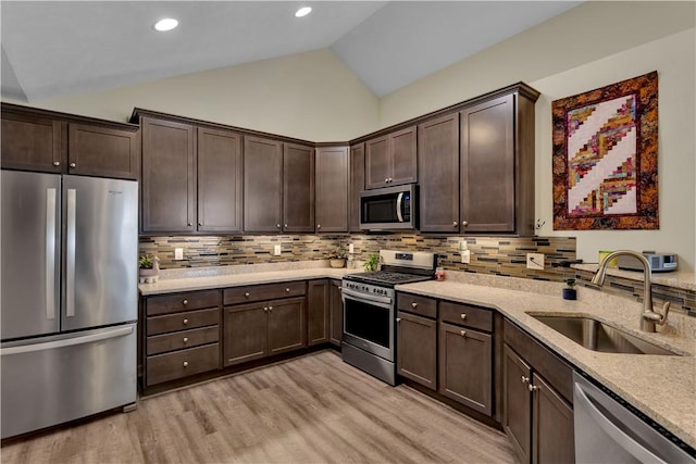 kitchen featuring appliances with stainless steel finishes, lofted ceiling, a sink, and dark brown cabinetry