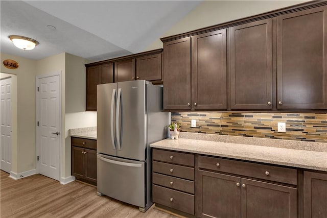 kitchen with light stone counters, decorative backsplash, light wood-style floors, freestanding refrigerator, and dark brown cabinetry