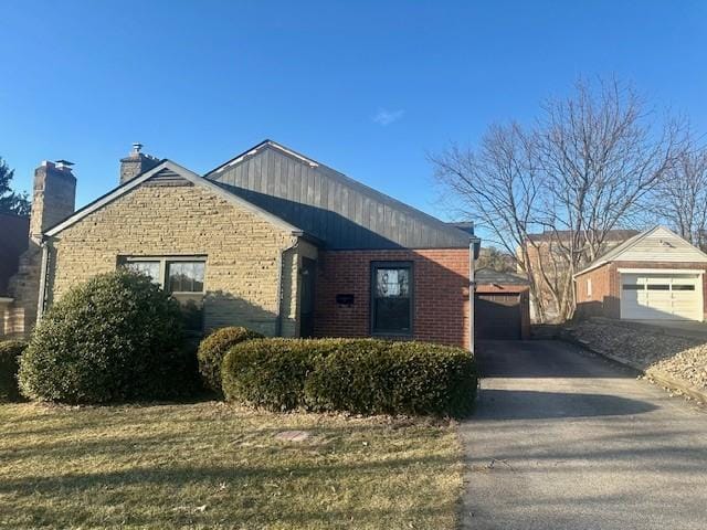 view of front of house with a garage, a chimney, an outdoor structure, and brick siding