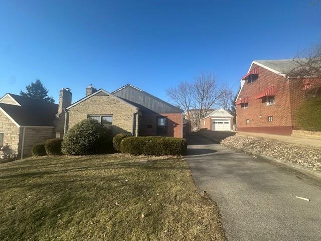 exterior space featuring driveway, a detached garage, a lawn, and an outdoor structure