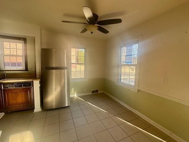 kitchen with light tile patterned flooring, visible vents, baseboards, freestanding refrigerator, and paneled dishwasher