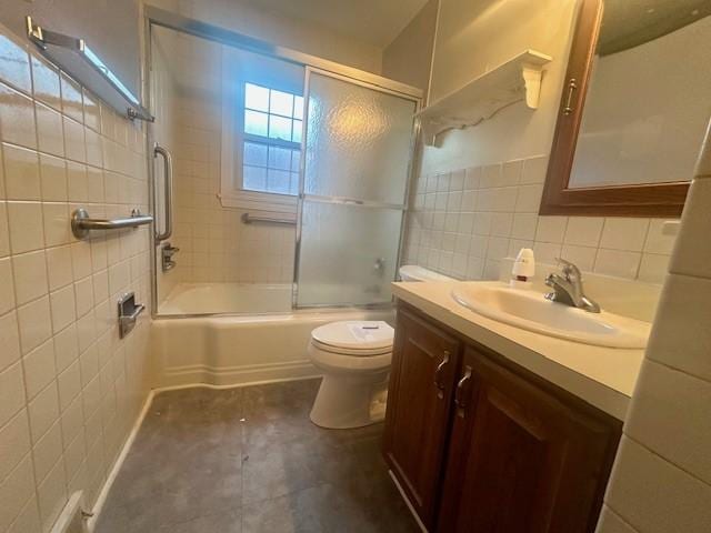 bathroom with combined bath / shower with glass door, tile walls, toilet, and vanity