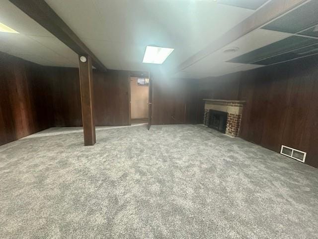 finished basement featuring carpet floors, a brick fireplace, wooden walls, and visible vents