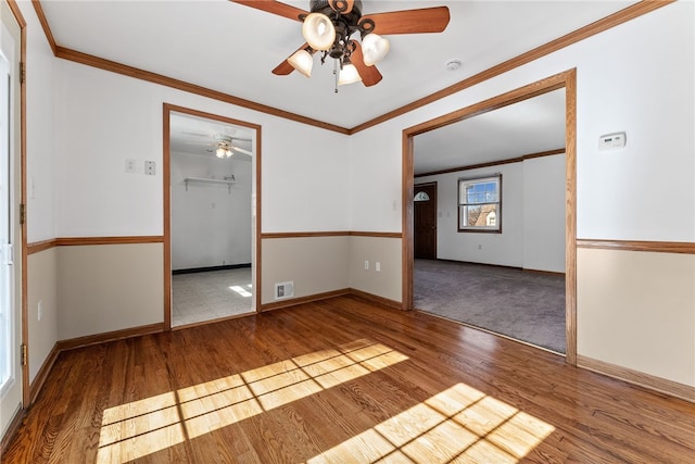 spare room with baseboards, wood finished floors, visible vents, and crown molding