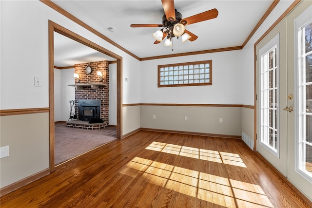 interior space with a healthy amount of sunlight, a wood stove, ornamental molding, and wood finished floors