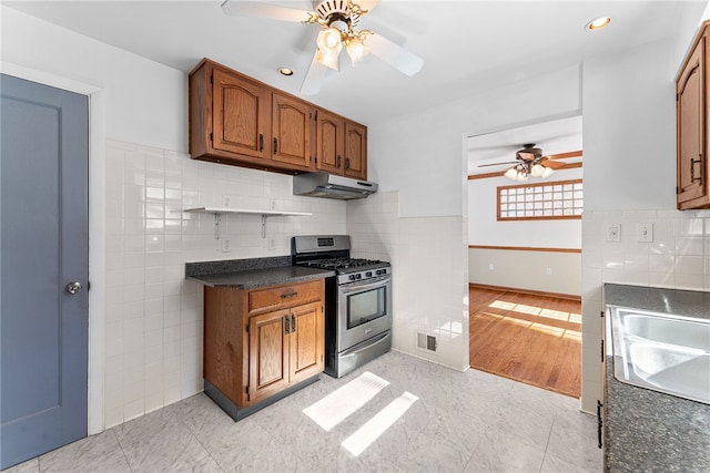 kitchen featuring stainless steel gas range oven, under cabinet range hood, a sink, visible vents, and dark countertops