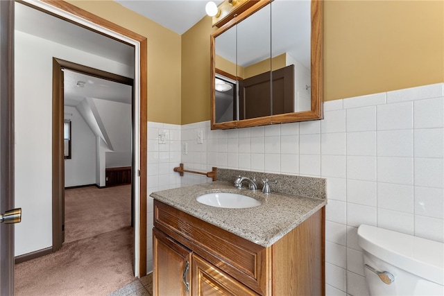 half bath featuring toilet, a wainscoted wall, vanity, and tile walls