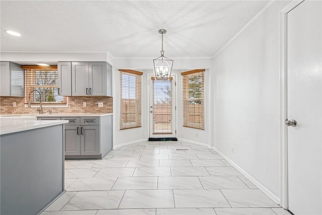 kitchen with a notable chandelier, tasteful backsplash, gray cabinets, light countertops, and ornamental molding