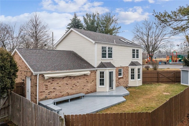 rear view of property featuring a playground, a fenced backyard, brick siding, roof with shingles, and a lawn