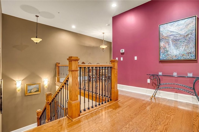 corridor with recessed lighting, wood finished floors, an upstairs landing, and baseboards