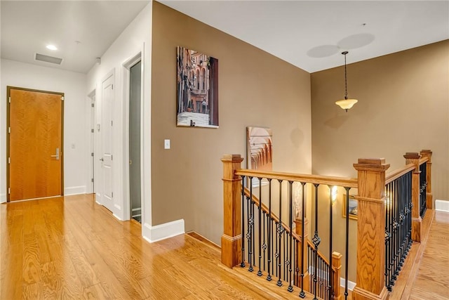 hallway featuring baseboards, visible vents, wood finished floors, and an upstairs landing