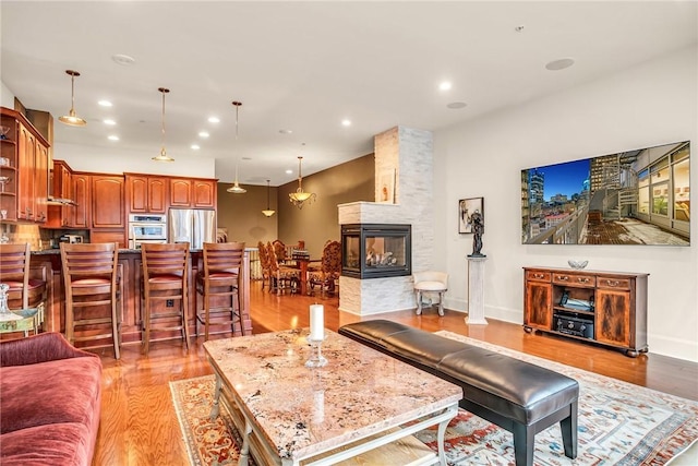 living room with baseboards, light wood-type flooring, a multi sided fireplace, and recessed lighting