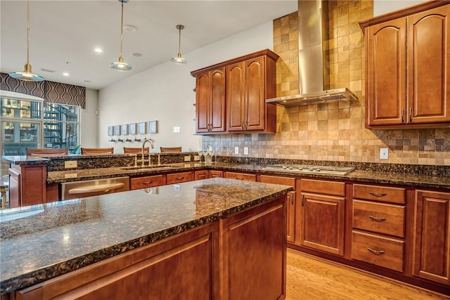 kitchen with a peninsula, a sink, wall chimney range hood, appliances with stainless steel finishes, and tasteful backsplash