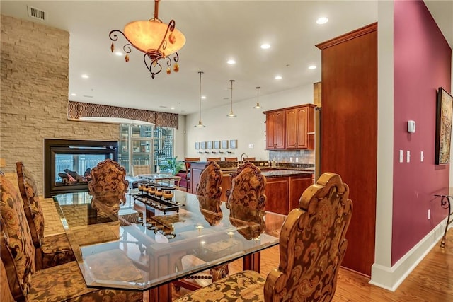 dining room with baseboards, visible vents, a stone fireplace, light wood-style floors, and recessed lighting