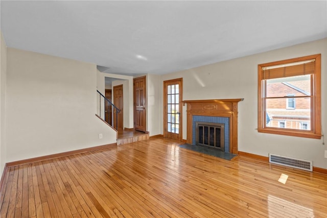 unfurnished living room featuring a tile fireplace, a healthy amount of sunlight, visible vents, and light wood-style flooring