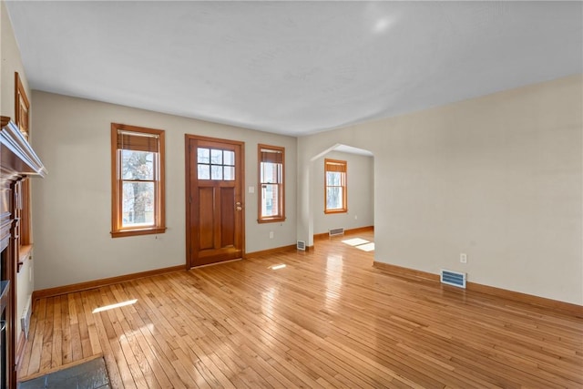 entryway featuring arched walkways, a fireplace, visible vents, light wood-type flooring, and baseboards