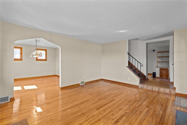 unfurnished living room with arched walkways, light wood finished floors, stairway, and visible vents