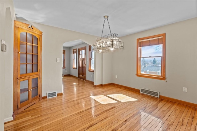 unfurnished dining area featuring light wood-style floors, visible vents, and arched walkways