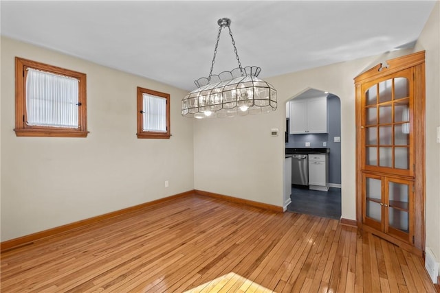 interior space with light wood-type flooring, arched walkways, and baseboards