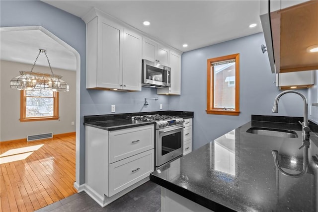 kitchen with visible vents, white cabinets, dark stone counters, appliances with stainless steel finishes, and a sink