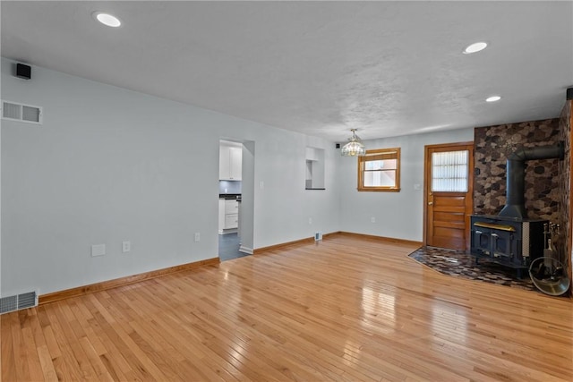 unfurnished living room with a wood stove, visible vents, light wood-style flooring, and baseboards