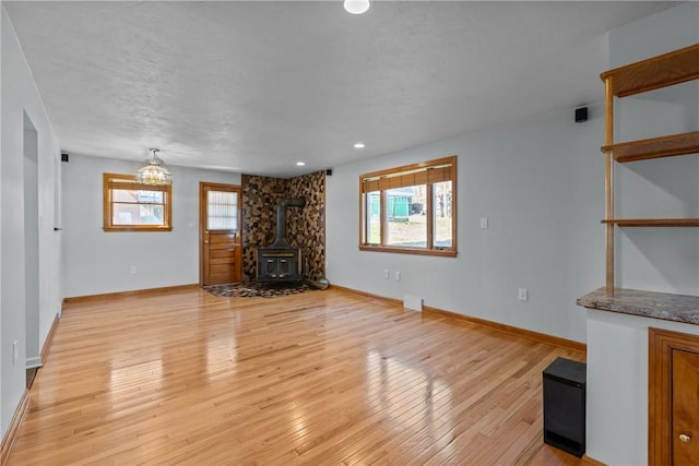 unfurnished living room featuring a wood stove, plenty of natural light, light wood-style flooring, and baseboards