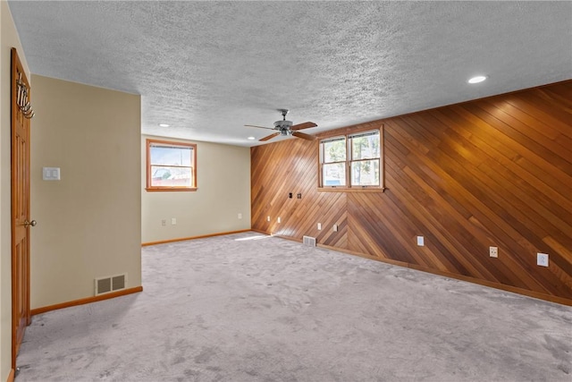 unfurnished room with visible vents, plenty of natural light, wood walls, and a textured ceiling