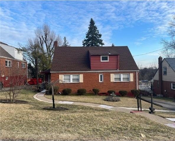 view of front of house with brick siding, a chimney, and a front yard