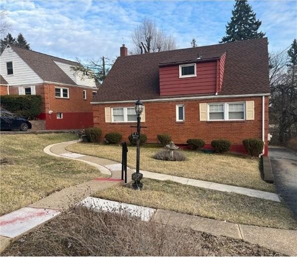 view of front of house with roof with shingles, brick siding, a chimney, and a front yard