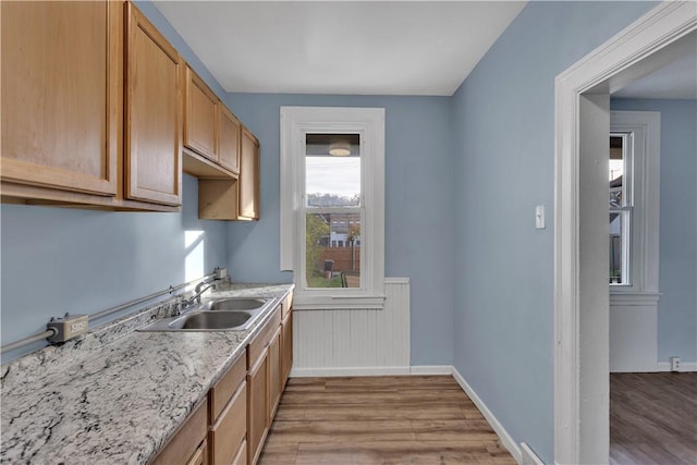 kitchen with a wainscoted wall, wood finished floors, a sink, light stone countertops, and baseboards