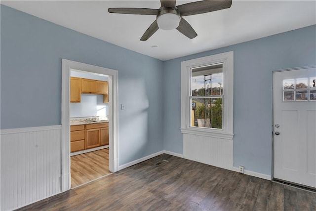 spare room with a wainscoted wall, a sink, wood finished floors, visible vents, and a ceiling fan