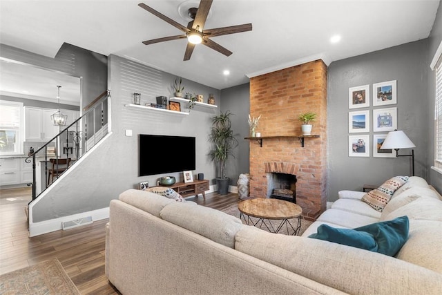 living room with visible vents, stairway, a brick fireplace, ceiling fan, and wood finished floors