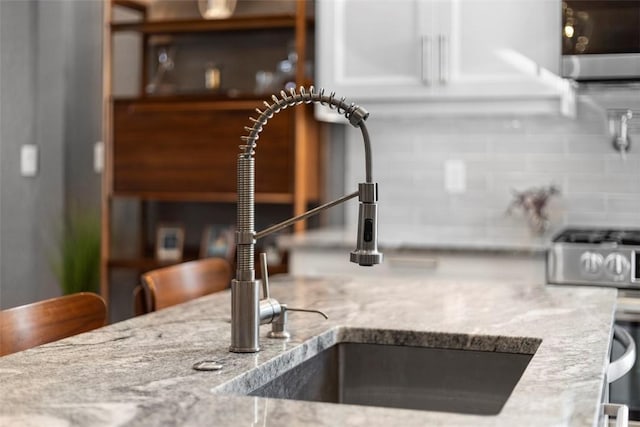 interior details featuring light stone countertops, gas range, decorative backsplash, and a sink