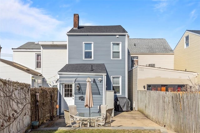 rear view of house with a fenced backyard, a chimney, and a patio