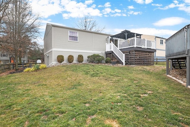 rear view of house with fence, a lawn, a deck, and stairs