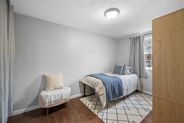 bedroom with a textured ceiling, baseboards, and wood finished floors