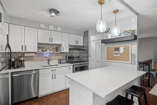 kitchen featuring under cabinet range hood, a peninsula, dark wood-type flooring, appliances with stainless steel finishes, and open shelves