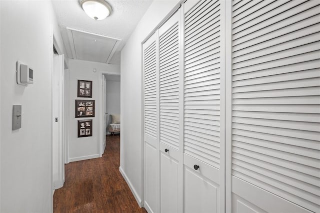 corridor featuring attic access, dark wood finished floors, a textured ceiling, and baseboards