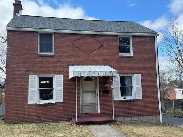 view of front facade featuring central AC unit, a chimney, a shingled roof, and brick siding