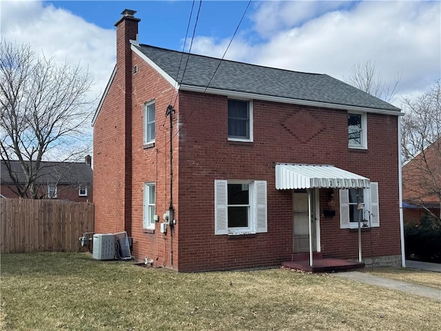 view of front facade featuring brick siding, a shingled roof, fence, a chimney, and a front yard