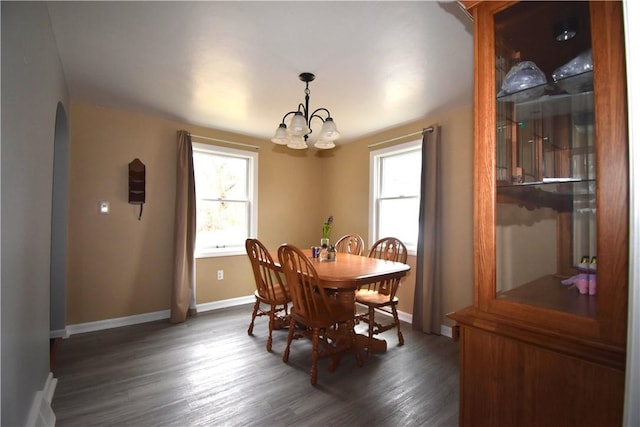 dining area with dark wood-type flooring, arched walkways, a chandelier, and baseboards