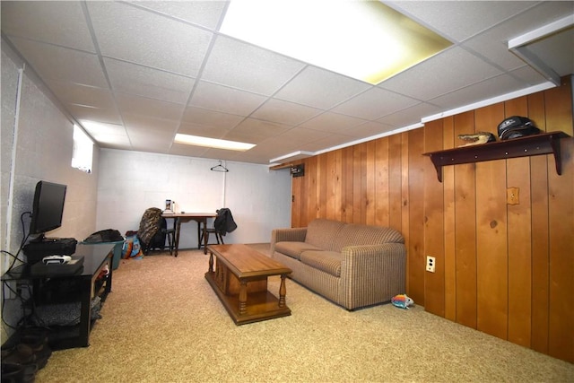 living area featuring carpet floors, concrete block wall, and a drop ceiling