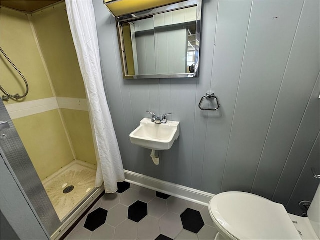 bathroom featuring a stall shower, baseboards, toilet, tile patterned flooring, and a sink